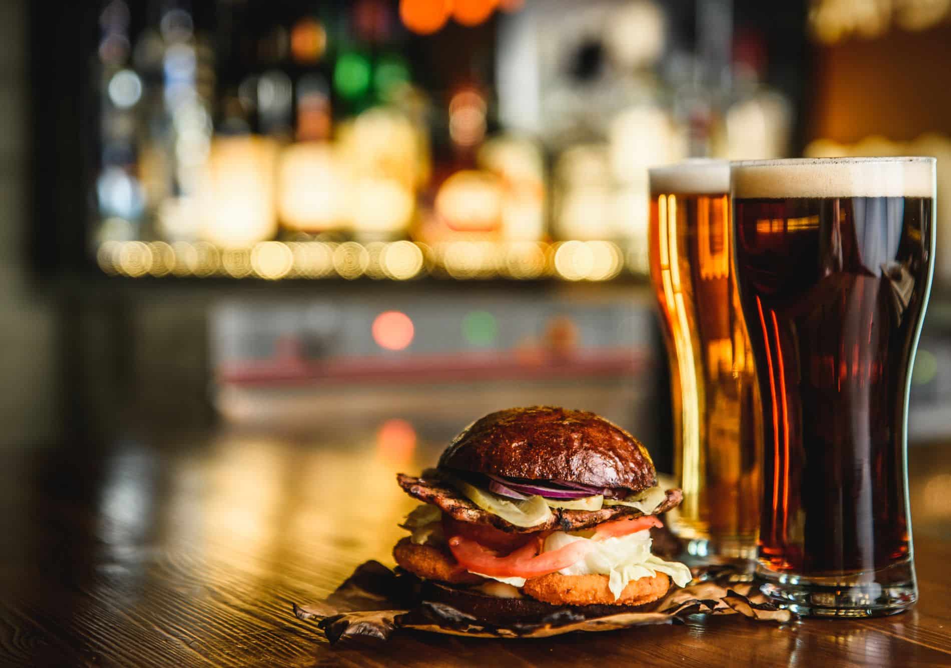 A juicy burger with two tall pints of beer on a table at a pub