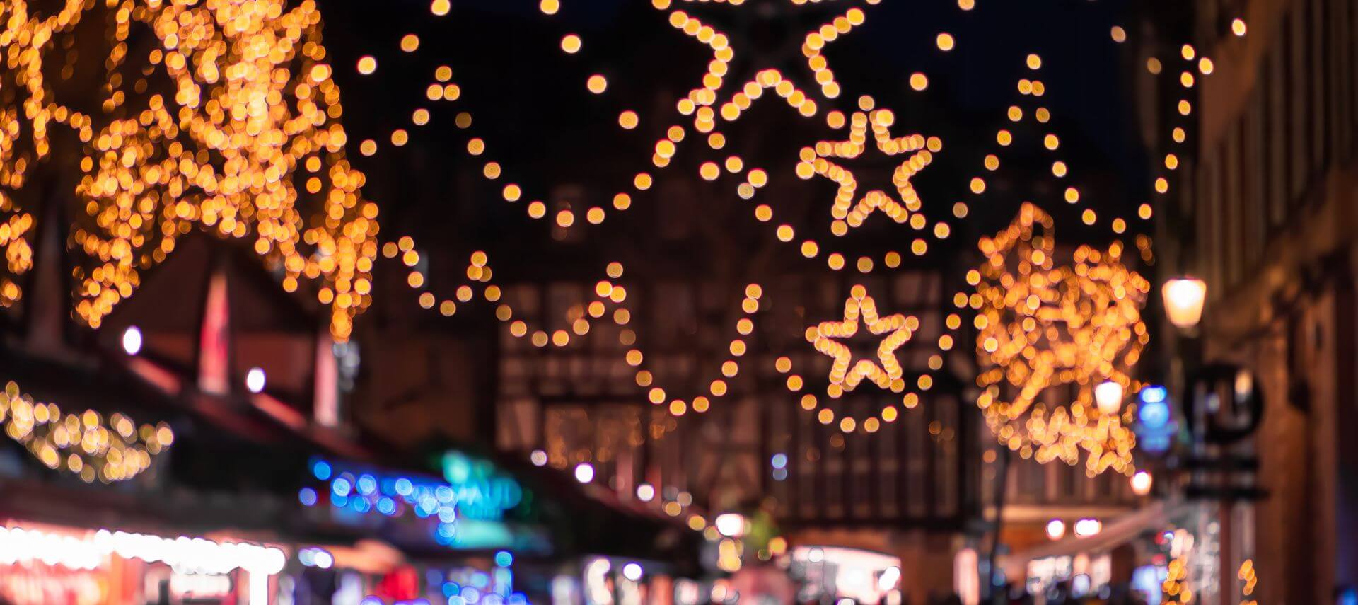 Strings of star shaped holiday lights glowing above a row of market stalls at night.