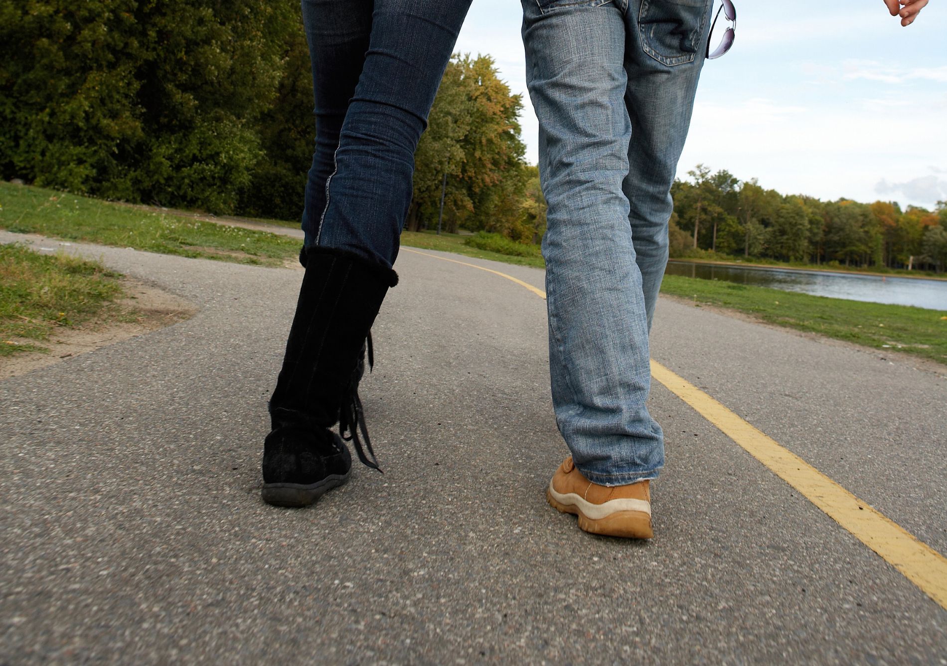 A couple walking on a paved path with water and trees in the background