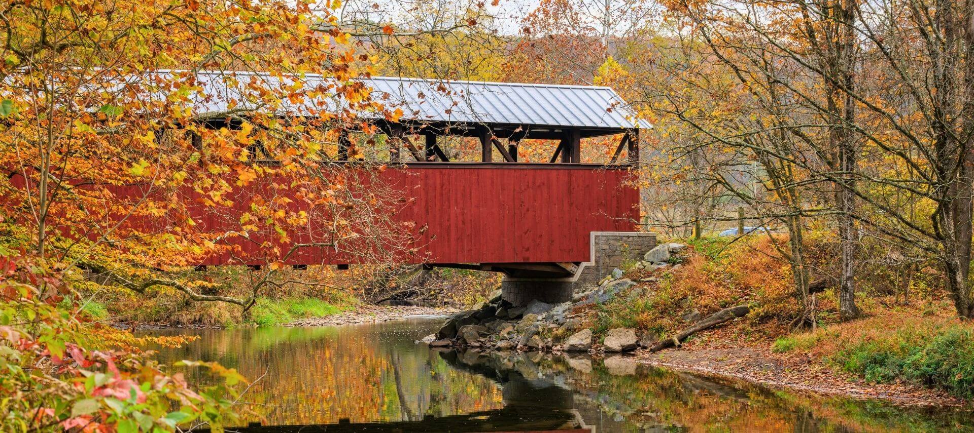 Red covered bridge crossing a creek surrounded by colorful fall foliage near Hershey, PA.