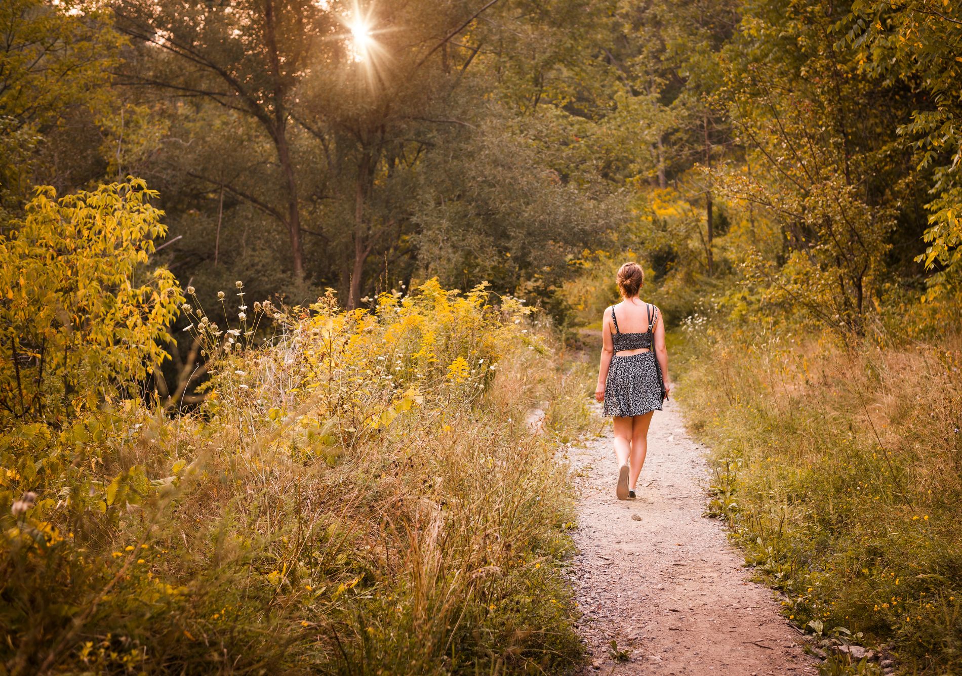 A woman in a dress is walking on a narrow path through the woods