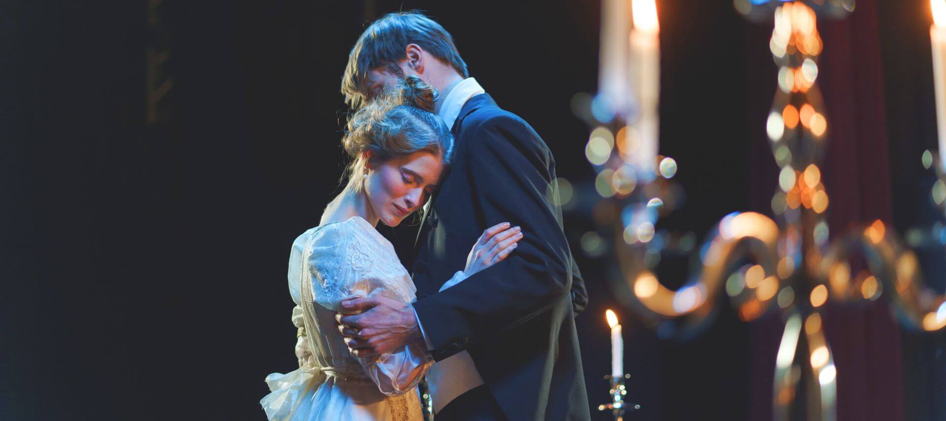 Man and woman in period costumes embracing on stage