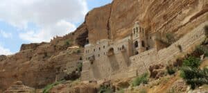 large stone fortress in desert surroundings with a tall stone wall behind it