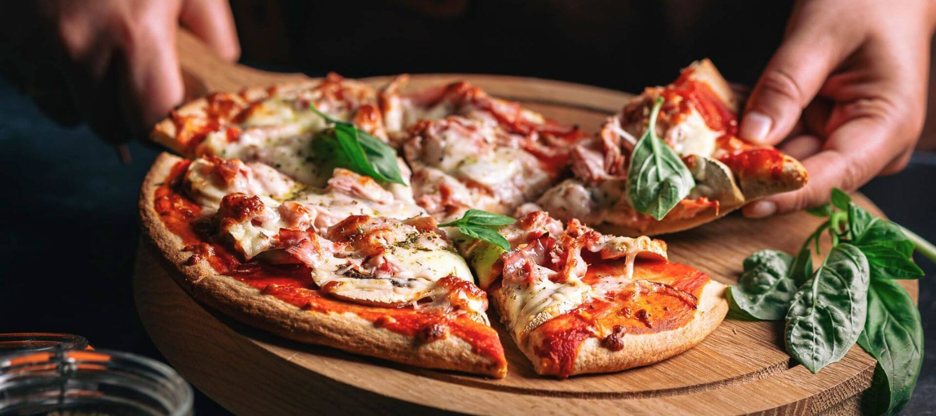 A freshly baked pizza topped with melted cheese, basil, and sliced meats on a wooden serving board.