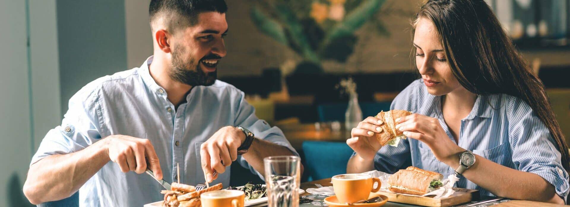 A couple enjoys sandwiches and coffee together at a cozy restaurant table during a casual dining outing.
