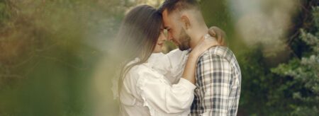 couple embracing outdoors with heads together, surrounded by soft greenery