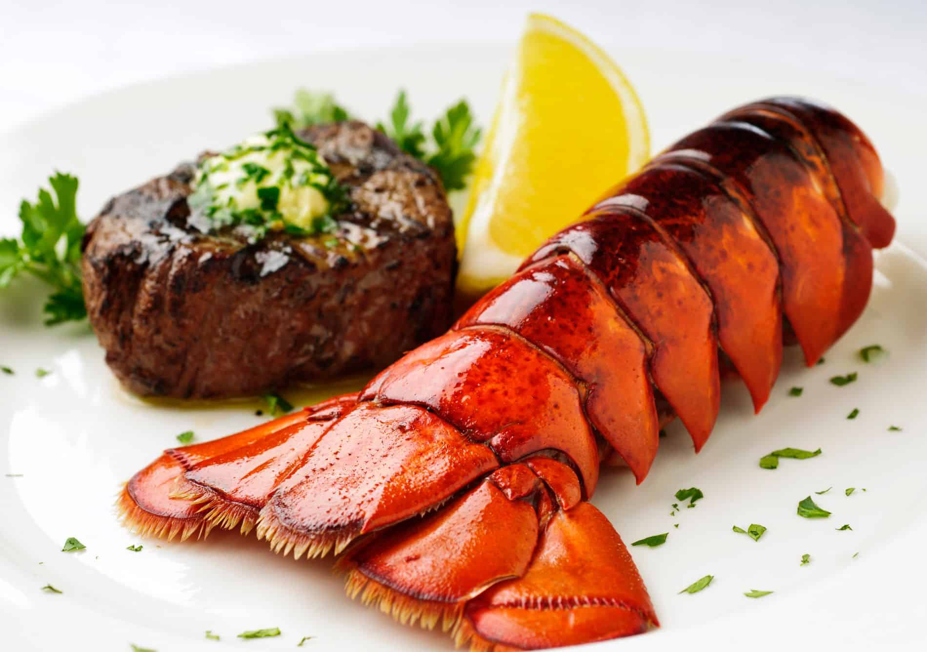 A plate of steak and lobster with a lemon wedge