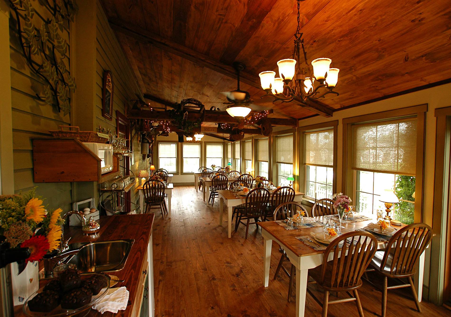 A dining room with wood floors and celings. Several tables in the room each have four plates with a yellow flower on all plates.